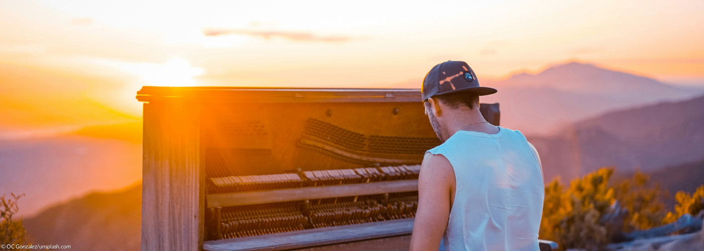 Titelbild für die Predigtreihe: Himmelsklang & Erdentöne - Ein Mann spielt auf einem Berg Klavier im Sonnenuntergang